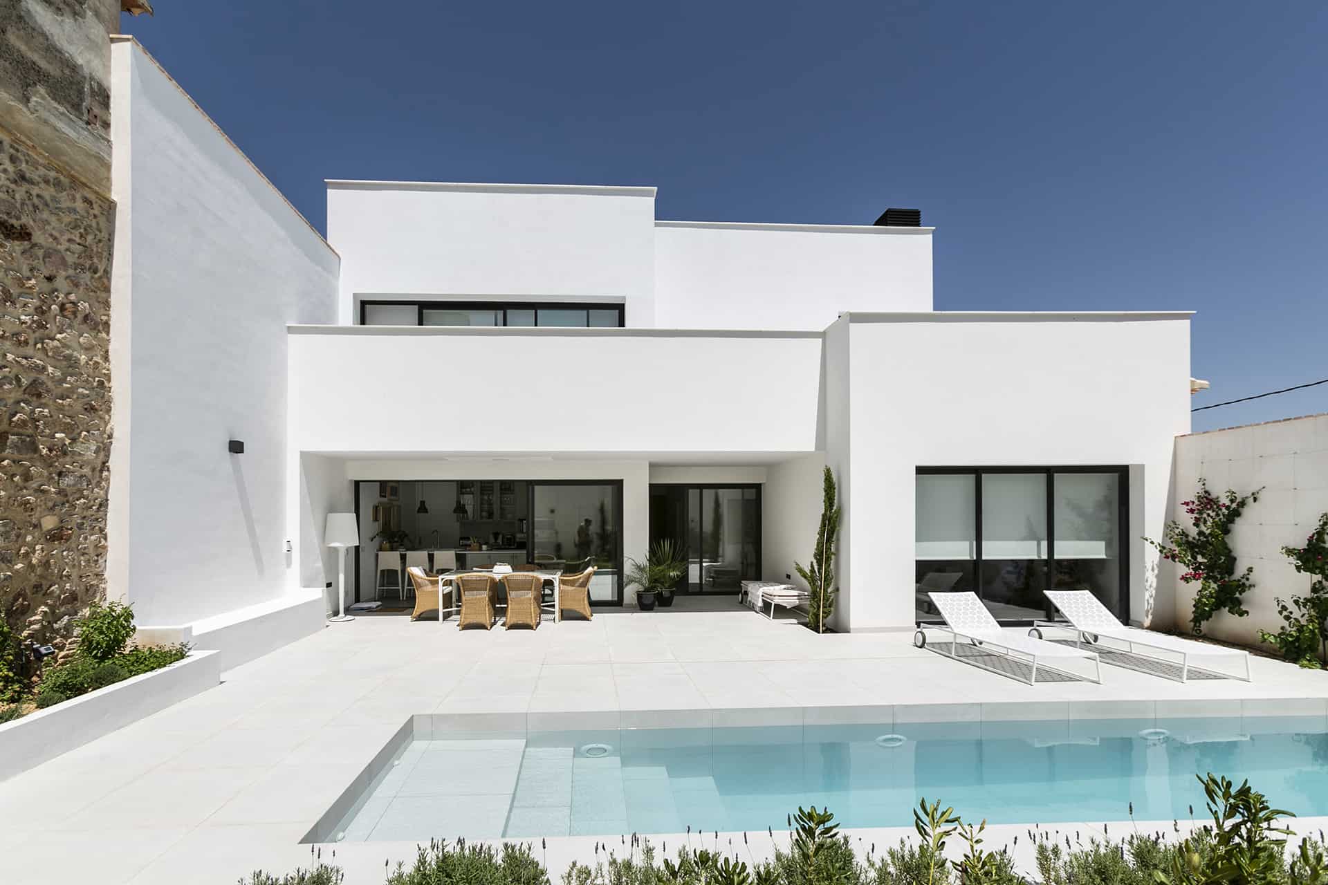 casa blanca estilo mediterranio de dos plantas y moderna con piscina de diseño y dos butacas para tomar el sol