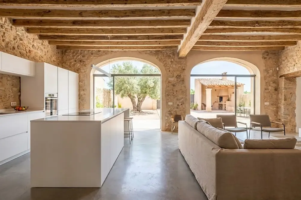 Salón de finca rústica rehabilitada en Benissa, mostrando contraste entre muros de piedra originales y mobiliario moderno.